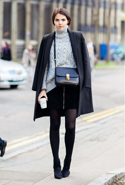 A cable knit sweater is worn with a draped black coat, miniskirt, tights, black heels, and a Céline bag