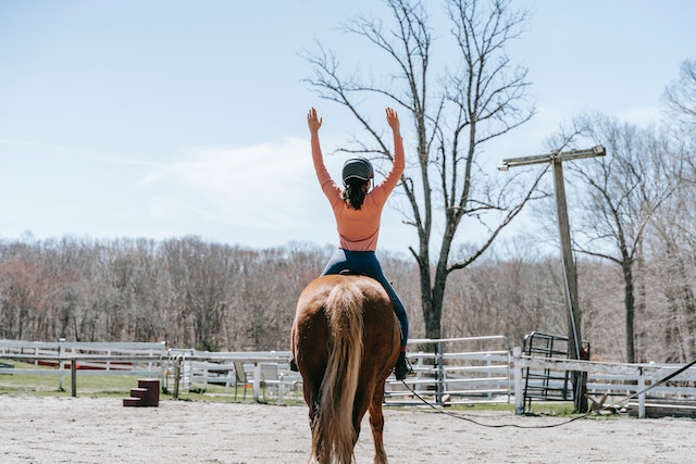 A girl riding a horse with her arms lifted
